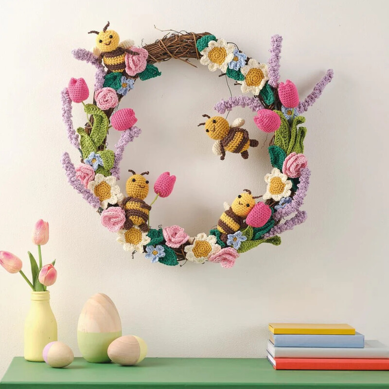 A spring wreath with crocheted flowers, leaves and bees on a wall. Clicking leads to all ideas and projects