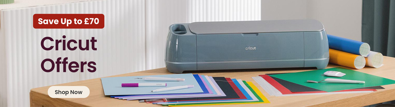 A table with a Cricut Maker 4 and tools and accessories. Header text says Save up to &pound;70 Cricut Offers, along with a Shop Now button. Clicking leads to Cricut products